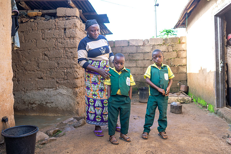 a Nigerian mother and her two boys standing between two homes