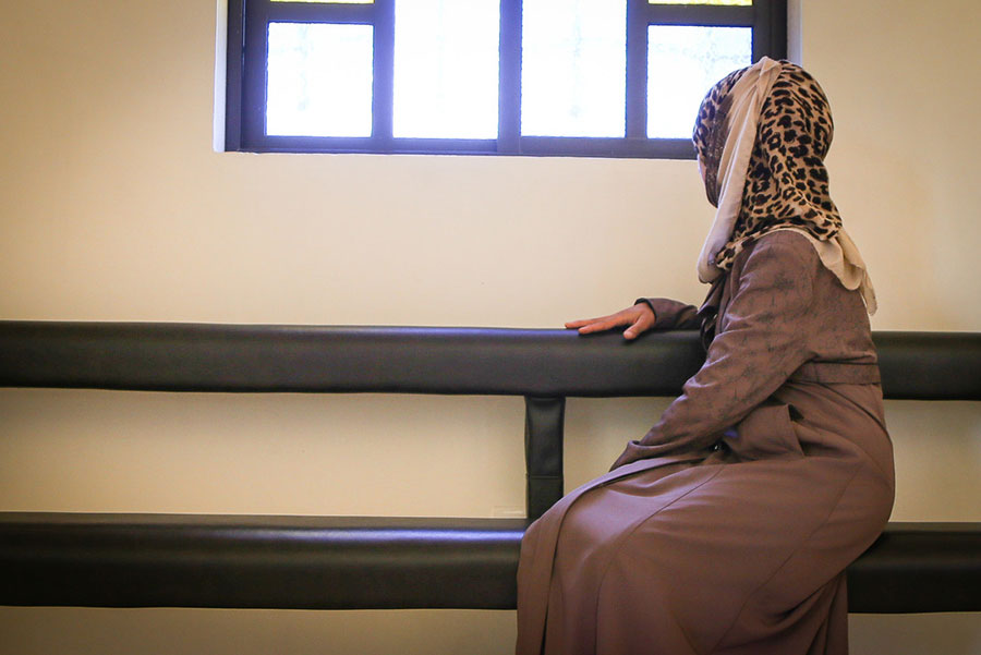 a woman in a headscarf and dress sitting on a bench and looking over her shoulder out a window