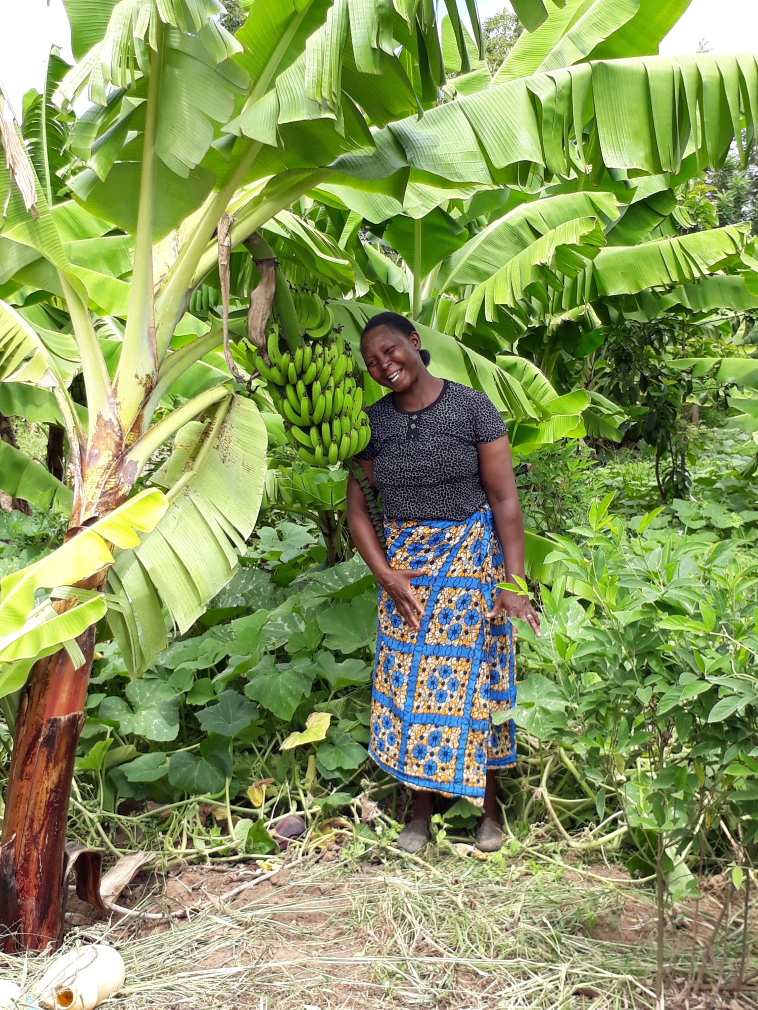 Smiling Black woman standing among trees and a bundle of bananas