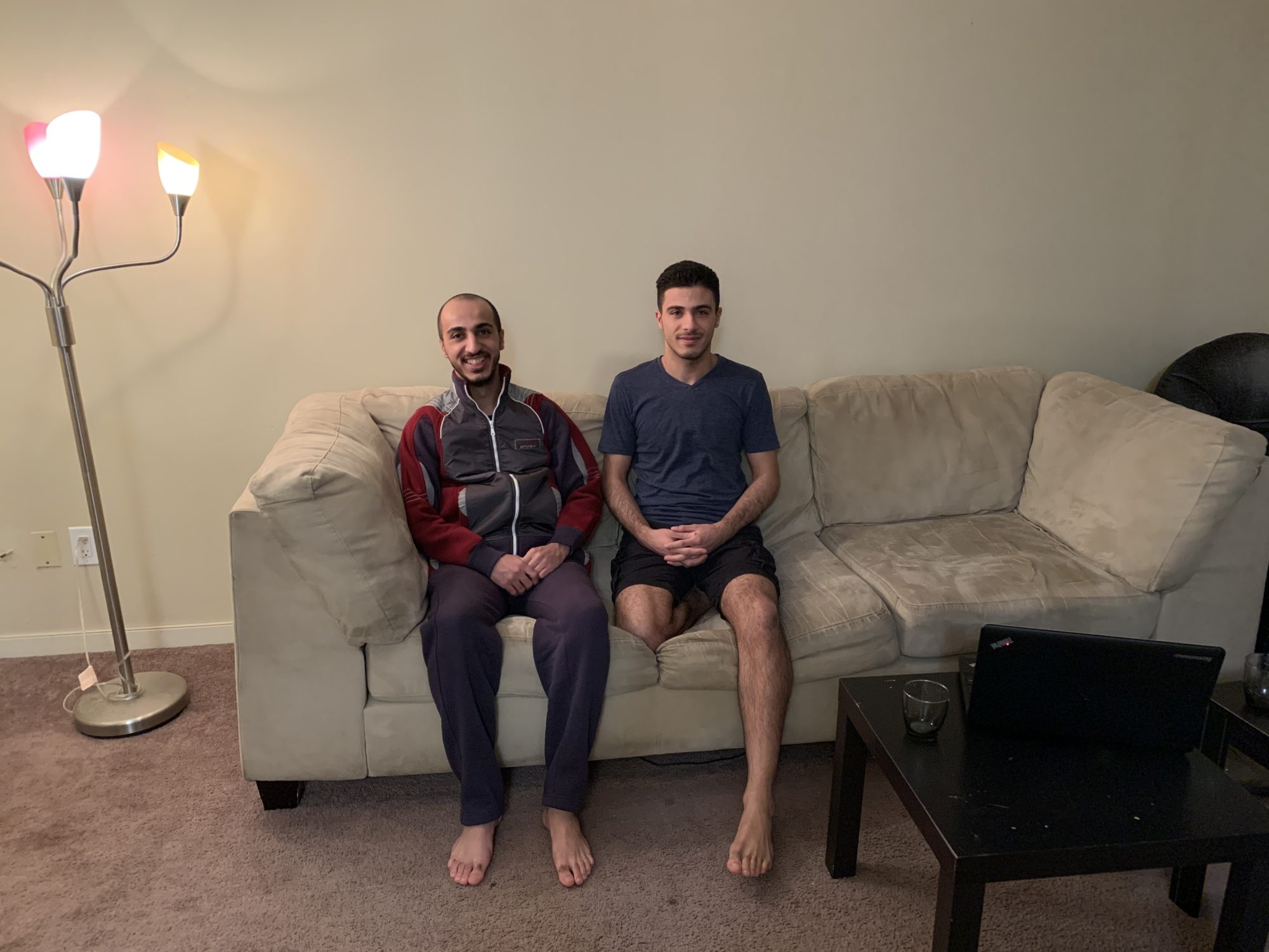 Two men sit beside one another smiling on a couch