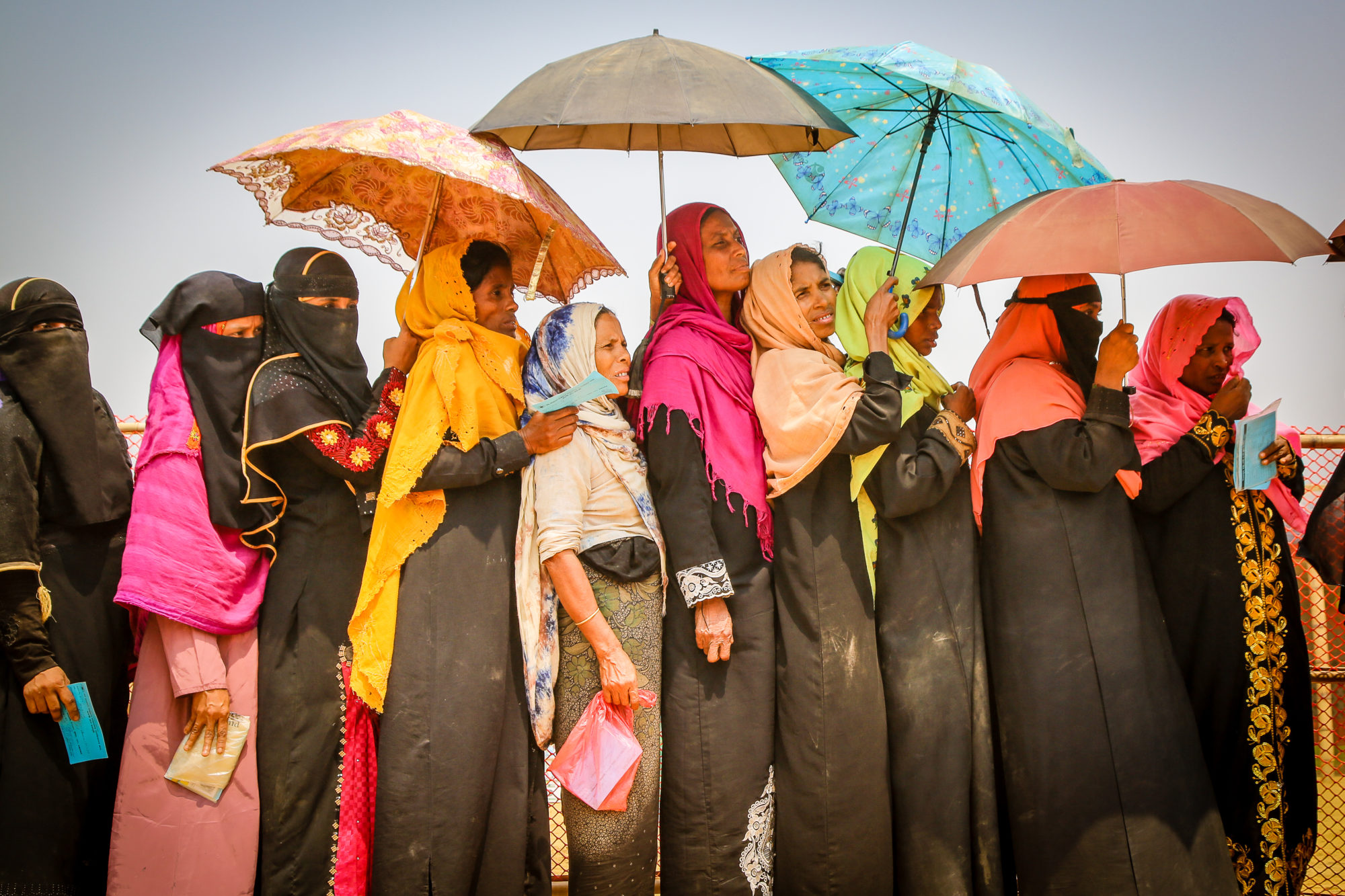a line of women in headscarves holding umbrellas to block the sun