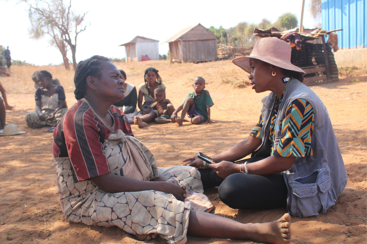 A mother sits with program staff on the ground.