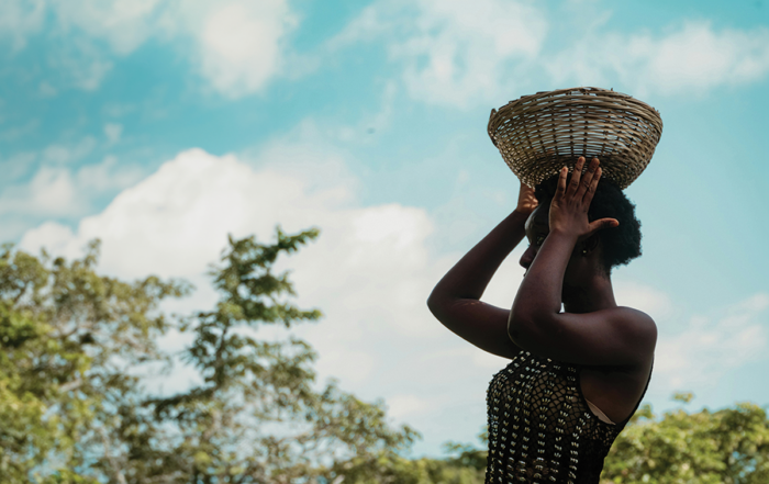 A woman carries a basket on her head.