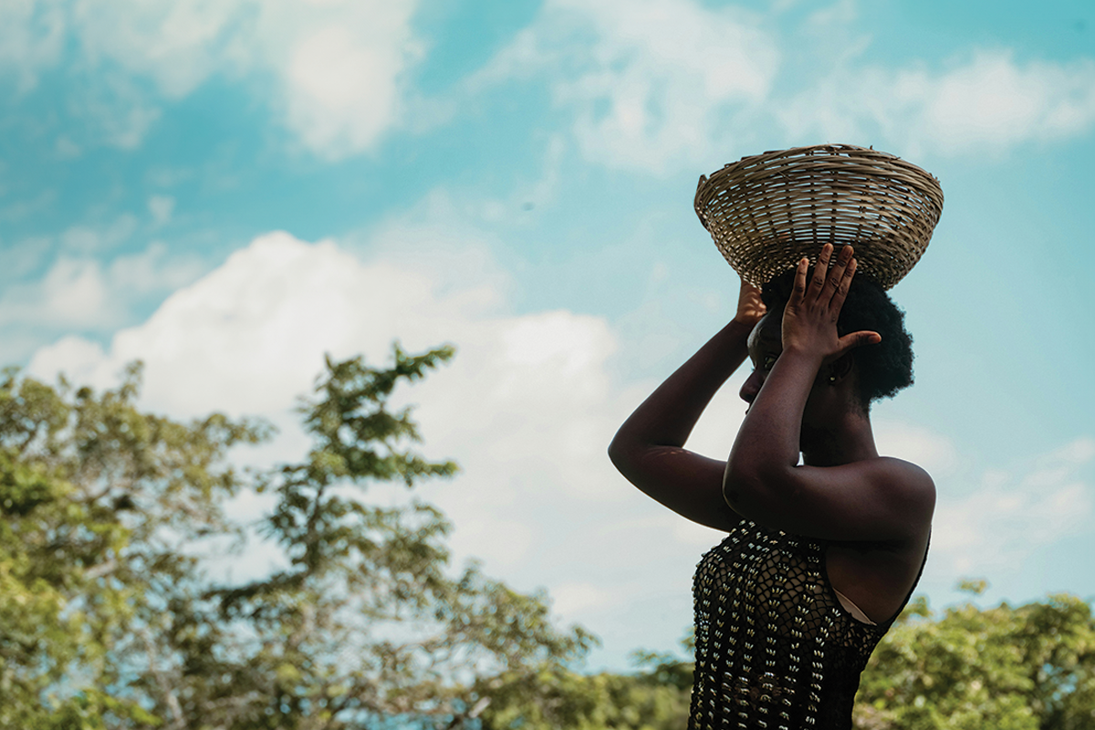 A woman carries a basket on her head.